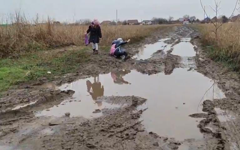 Дети добираются домой со школы через лужи, не всегда удается удержаться на такой дороге и не упасть в грязь